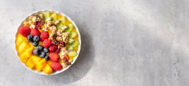 Sağlıklı, yaban mersini, ahududu, kivi ve tahıl gevreğiyle saglikli mango smoothie kasesi. Açık gri ahşap arkaplanda fotokopi alanı olan bir manzara üstünde 