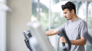 Genç yetişkin, yoğun eliptik kardiyo seansı sırasında derinden odaklanmış.