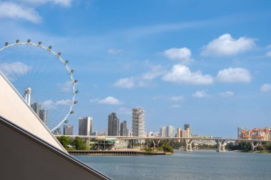 Singapur Flyer, liman ve ön planda bir köprü ile modern bir şehir siluetine karşı dimdik ayakta duruyor. Kentsel mimari ve mühendisliğin panoramik görüntüsü. .