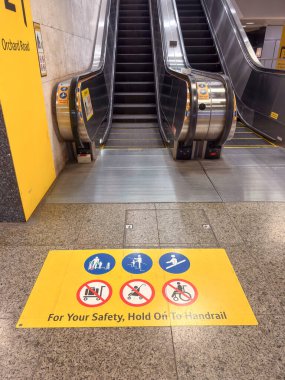 Singapur, Singapur - 1 Mayıs 2025: yürüyen merdivendeki sarı işaret tırabzanları tutmak için ikonlar içeren bir güvenlik öneriyor. Yakınlarda, yürüyen merdivenler yukarı aşağı hareket ediyor..