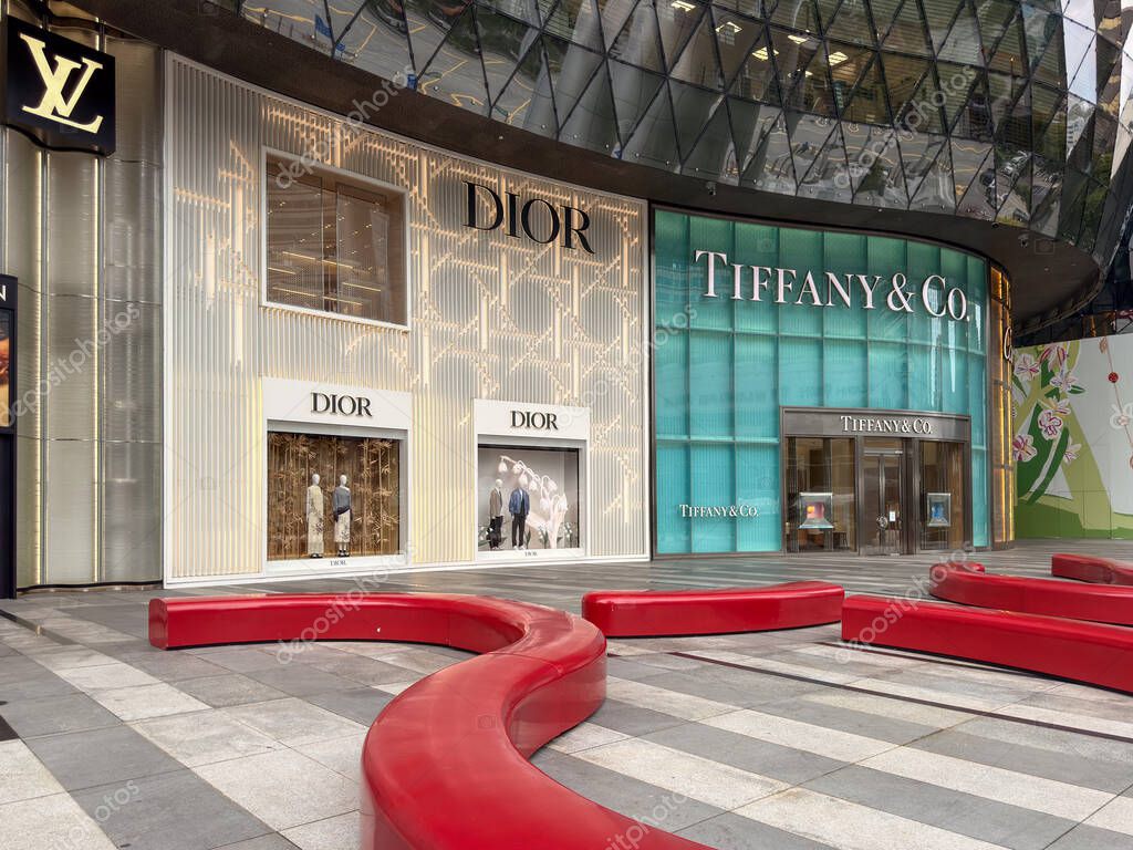 Singapore, Singapore - May 1, 2025: luxury storefronts of DIOR and TIFFANY and CO. visible, with distinctive architecture and red seating in the foreground creating a shopping environment.