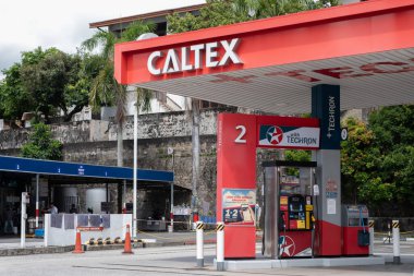 Penang, Malezya - 15 Nisan 2025: Kırmızı bir gölgelik ve bir benzin istasyonunun bulunduğu bir Caltex benzin istasyonu. Bölge yeşillik ve arka plandaki konut binalarıyla çevrili..