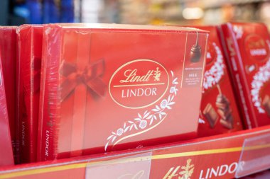  Lindt Lindor sütlü çikolata kutuları, parlak kırmızı ambalajlar ve çekici görsellerin yer aldığı bir perakende satış ortamında düzenlenmiştir.