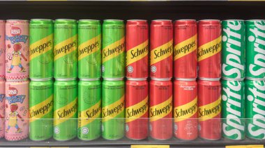  Schweppes ve Sprite de dahil olmak üzere renkli içecek kutuları bir süpermarket rafında dizilmiş, çeşitli aromalar ve tasarımlar sergiliyorlar..