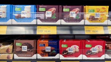  Raflara yerleştirilmiş koyu çikolata, kakao mus ve badem ezmesi gibi çeşitli Ritter çikolata ürünlerinin renkli ambalajları.