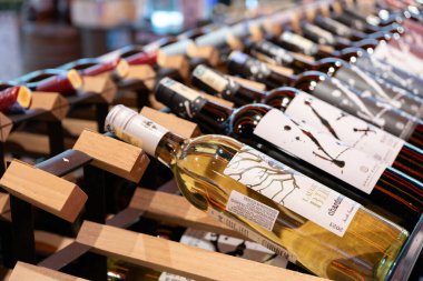  çeşitli şarap şişeleri ahşap raflarda düzgünce düzenlenir. Etiketlerde farklı tasarımlar ve şarap türleri yer alıyor, müşteriler için bir seçim sunuluyor.