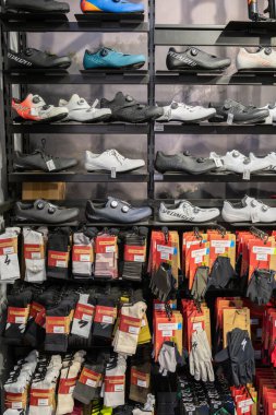 Penang, Malezya 15 Nisan 2025 'te bir duvar ekranında farklı stil ve renklerde sıralanmış bisiklet ayakkabıları, eldivenler ve altında asılı diğer bisiklet takımları sergilenmektedir..