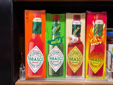 Penang, Malezya - 7 Temmuz 2025: Her biri özel ciltlerle etiketlenmiş hafif, sarımsak ve sıcak gibi çeşitli acı biber sosu şişeleri art arda dizilmiştir..