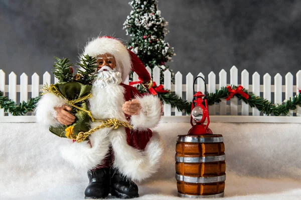 在水平的圣诞场景中 圣诞老人手持礼物站在树前的雪地里 — 图库照片