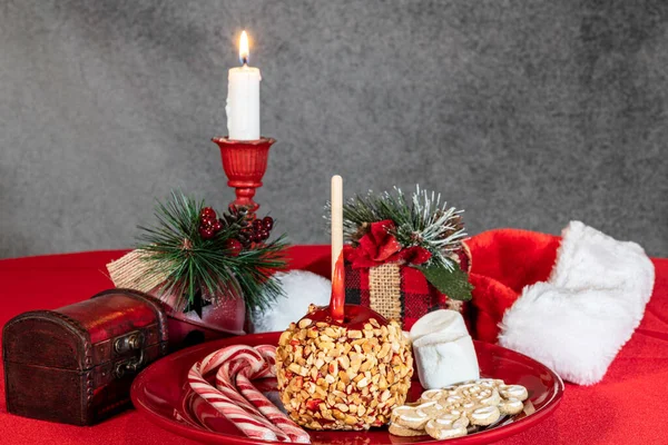 圣诞糖果苹果糖果手杖姜饼和棉花糖在红盘上 点着蜡烛和节日装饰品 — 图库照片