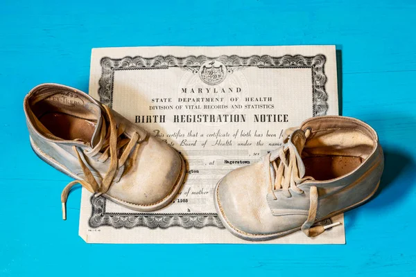 old Maryland birth certificate and vintage white baby shoes on blue background