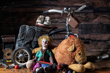 Tavan arasında eski oyuncaklar, siyah ahşap arka planda, üç tekerlekli bisiklet, doldurulmuş aslan ve beyaz bebek ayakkabıları da dahil.
