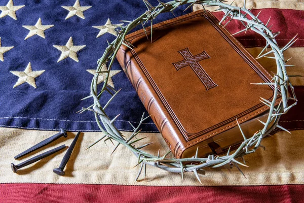 leather bible and crown of thorns on American flag with old rose head nails