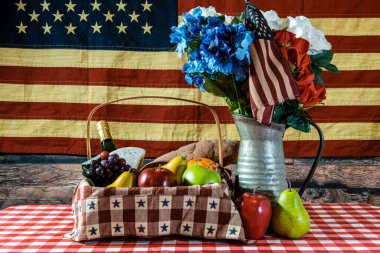 picnic basket on checkered table cloth bouquet of flowers and American flag background clipart