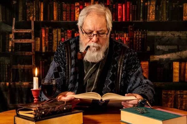 stock image senior male Caucasian reading book and smoking pipe in retro looking library with glass on wine