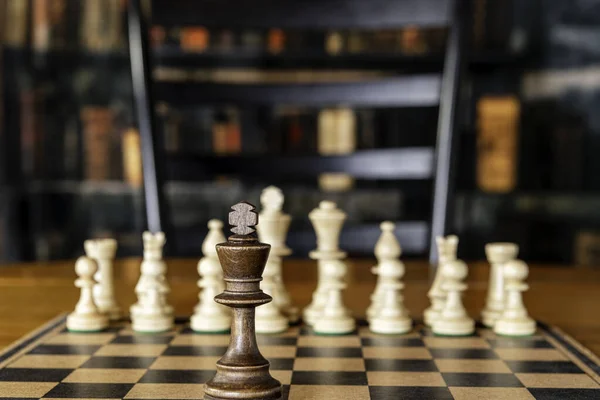 chess board on wood table in library with one king isolated against opposing army