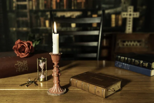 Bibles on wood table with one burning candle with out of focus old library background