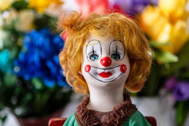Turuncu saçlı, bahar çiçeği arka planında kırmızı burunlu antika palyaço bebeği.