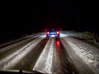 A car drives slowly at night on a slippery snowy road in the USA