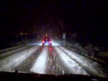 A car drives slowly at night on a slippery snowy road in the USA