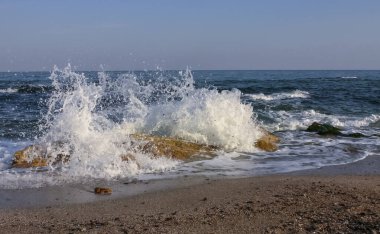 Waves break on a stone and white splashes of water fly into the air, the Black Sea
