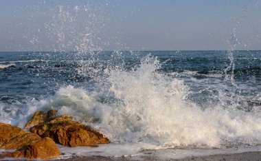 Waves break on a stone and white splashes of water fly into the air, the Black Sea