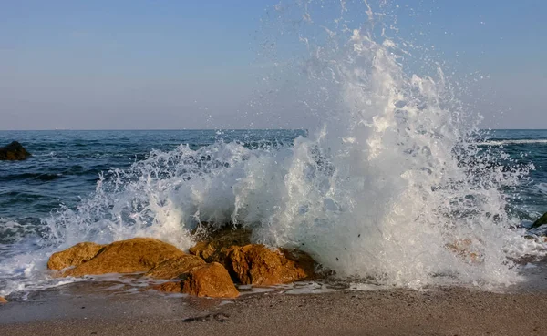 Waves break on a stone and white splashes of water fly into the air, the Black Sea