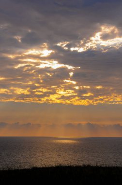 Denizin üzerinde renkli turuncu gün doğumu, bulutlarda güneş ışığı