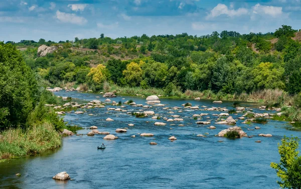 Lastik bir teknede bir balıkçı Ukrayna 'nın güneyindeki Bug Nehri' nin ortasındaki kaya yarıklarının arkasında balık yakalar.