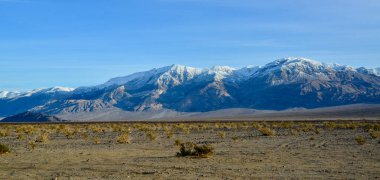 Kaliforniya 'daki Ölüm Vadisi bölgesinde kışın ıslak kil çöl manzarası karla kaplı dağlar karşısında.