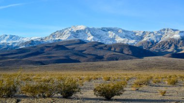 Kaliforniya 'daki Ölüm Vadisi bölgesinde kışın ıslak kil çöl manzarası karla kaplı dağlar karşısında.