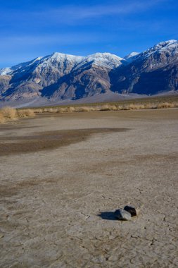 Kaliforniya 'daki Ölüm Vadisi bölgesinde kışın ıslak kil çöl manzarası karla kaplı dağlar karşısında.