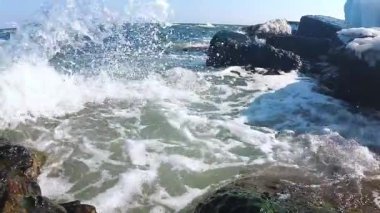 Suda hava kabarcıkları olan dalgalar akın ediyor. Video kamera ve taşlar midye ve alglerle kaplanıyor.