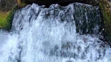 Köpüklü ve hava kabarcıklı temiz bir su akıntısı eski bir demir borudan akar ve taşları yeşil alglerle yıkar.