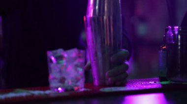 4K profesyonel barmen kokteyl bardağından barın tezgahına karışık mavi likör kokteyli dolduruyor. Barmen müşteriye alkol servisi yapıyor.
