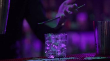 4K profesyonel barmen kokteyl bardağından barın tezgahına karışık mavi likör kokteyli dolduruyor. Barmen müşteriye alkol servisi yapıyor.