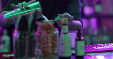 4K profesyonel barmen kokteyl bardağından barın tezgahına karışık mavi likör kokteyli dolduruyor. Barmen müşteriye alkol servisi yapıyor.