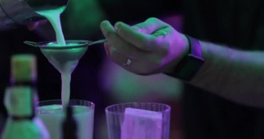 4K profesyonel barmen kokteyl bardağından barın tezgahına karışık mavi likör kokteyli dolduruyor. Barmen müşteriye alkol servisi yapıyor.