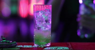 4K profesyonel barmen kokteyl bardağından barın tezgahına karışık mavi likör kokteyli dolduruyor. Barmen müşteriye alkol servisi yapıyor.