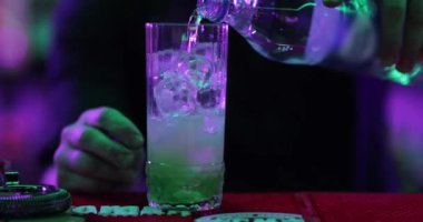 4K profesyonel barmen kokteyl bardağından barın tezgahına karışık mavi likör kokteyli dolduruyor. Barmen müşteriye alkol servisi yapıyor.