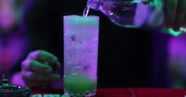 4K profesyonel barmen kokteyl bardağından barın tezgahına karışık mavi likör kokteyli dolduruyor. Barmen müşteriye alkol servisi yapıyor.