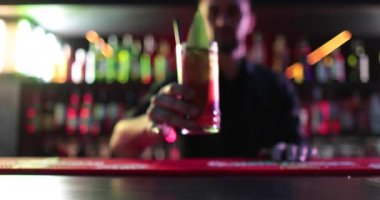 4K profesyonel barmen kokteyl bardağından barın tezgahına karışık mavi likör kokteyli dolduruyor. Barmen müşteriye alkol servisi yapıyor.