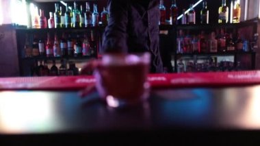 4K profesyonel barmen kokteyl bardağından barın tezgahına karışık mavi likör kokteyli dolduruyor. Barmen müşteriye alkol servisi yapıyor.