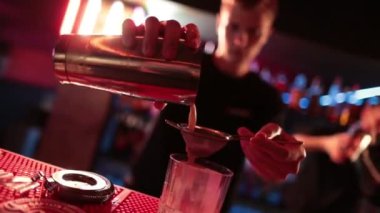 4K profesyonel barmen kokteyl bardağından barın tezgahına karışık mavi likör kokteyli dolduruyor. Barmen müşteriye alkol servisi yapıyor.