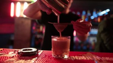 4K profesyonel barmen kokteyl bardağından barın tezgahına karışık mavi likör kokteyli dolduruyor. Barmen müşteriye alkol servisi yapıyor.