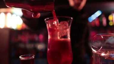 4K profesyonel barmen kokteyl bardağından barın tezgahına karışık mavi likör kokteyli dolduruyor. Barmen müşteriye alkol servisi yapıyor.