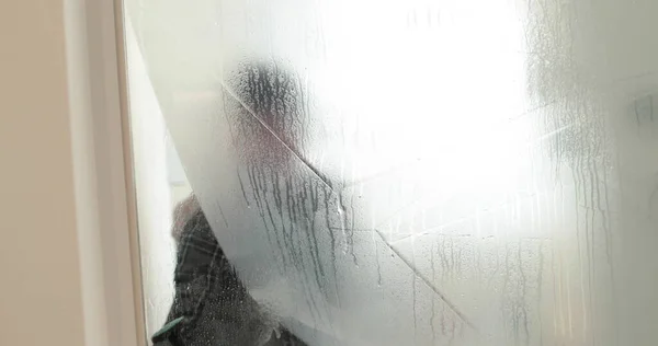 A man pastes a frosted coating on a glass door in a clinic to make the glass door opaque. Applying a matte coating to the glass.
