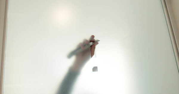 Мужчина наклеивает глазированное покрытие на стеклянную дверь в клинике, чтобы сделать стеклянную дверь непрозрачной. Применение матового покрытия к стеклу.