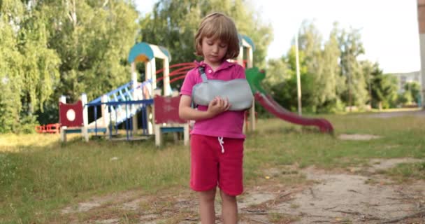 壊れた手足の小さな傷ついた少年と屋外で悲しい子供 子供は腕が折れている 腕のバンデージ — ストック動画