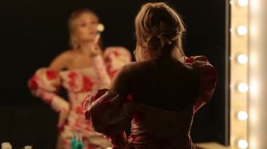 Kırmızı dudaklı ve gözlüklü güzel kadın makyajını düzeltiyor. Evdeki ya da otel odasındaki aynaya bakıyor.